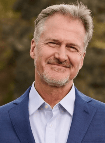 The image is of Chad Cook, a physiotherapist from the USA. He is wearing a white shirt and a blue blazer. 